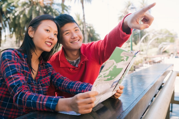 Retrato de casal de viajantes asiáticos feliz segurando um mapa e procurando direções. Conceito de viagens e férias.