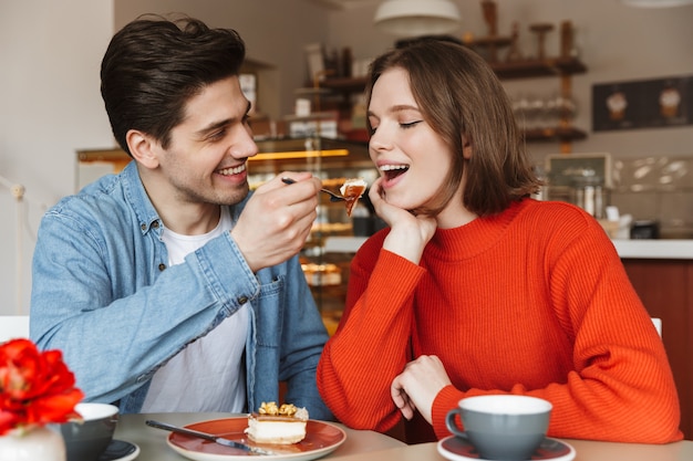 Retrato de casal feliz namorando, enquanto homem alimentando mulher com bolo saboroso em uma padaria aconchegante