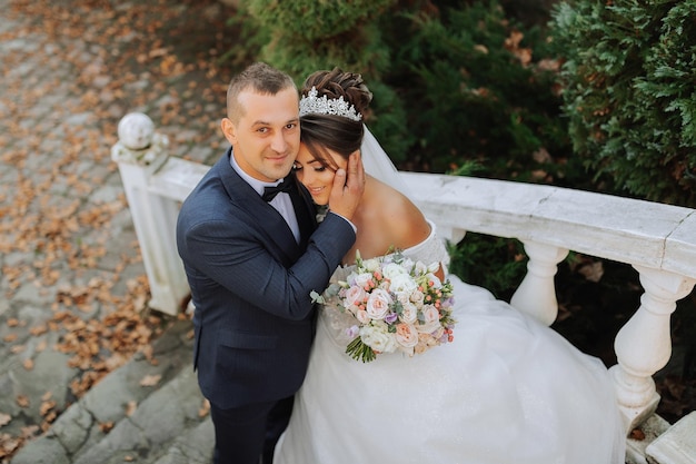 retrato de casal feliz no casamento noiva e noivo no parque da floresta de outono posando perto de escadas de pedra um homem de terno uma menina de vestido de noiva noivo beija sua namorada foto de cima