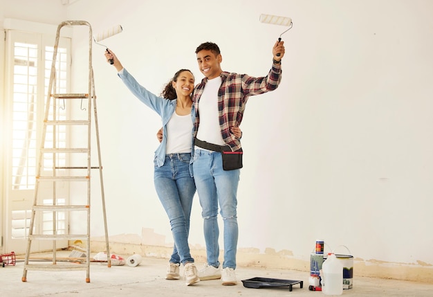 Retrato de casal feliz pintando a nova sala de estar em uma casa ou apartamento Homem e mulher com pincel para decorar uma cor de parede e renovar o interior da casa com sorriso ou felicidade juntos