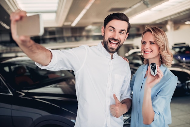 Retrato de casal feliz tomando selfie no smartphone com as chaves do carro novo