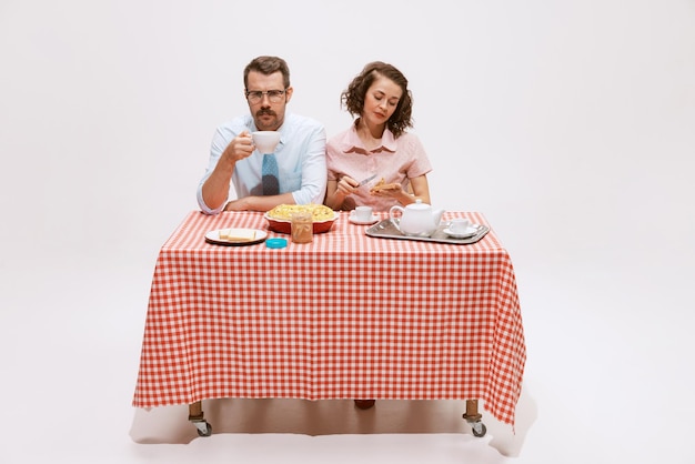 Retrato de casal homem e mulher sentados à mesa tomando café da manhã saboroso isolado no branco