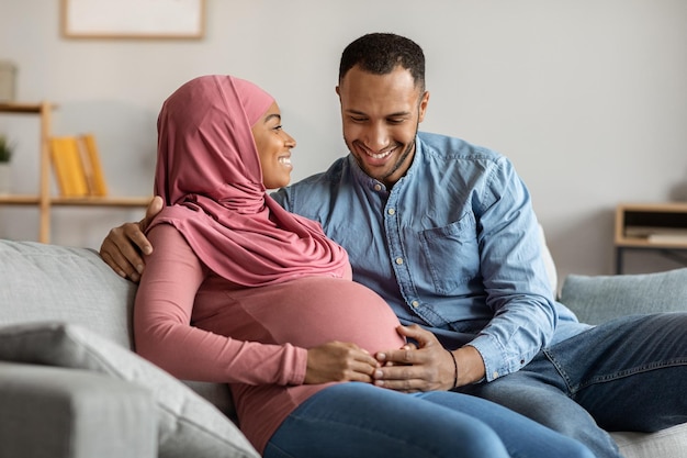 Retrato de casal islâmico feliz esperando bebê relaxando juntos em casa