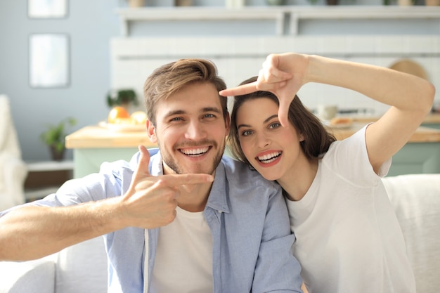 Retrato de casal jovem bonito, apontando e rindo, sentado no sofá.