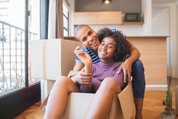 Retrato de casal latino feliz se divertindo com caixas de papelão na casa nova no dia da mudança