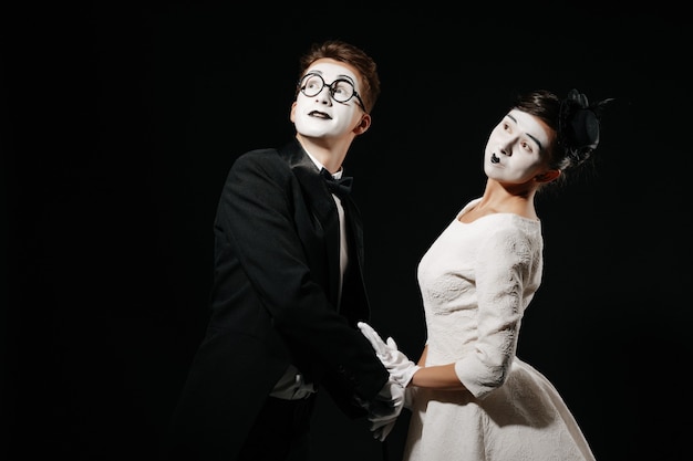 Retrato de casal mímica em fundo preto. homem de smoking e óculos e mulher de vestido branco