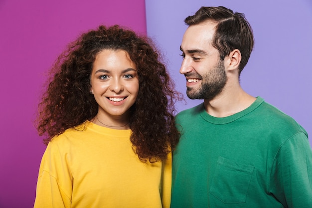 Foto retrato de casal moreno caucasiano em roupas coloridas, sorrindo juntos, homem olhando para mulher isolada