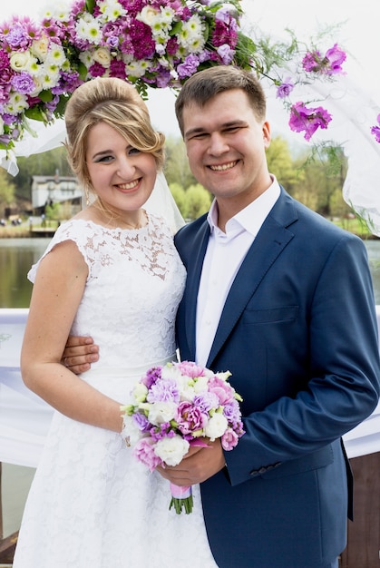 Retrato de casal recém-casado posando sob o arco decorativo floral