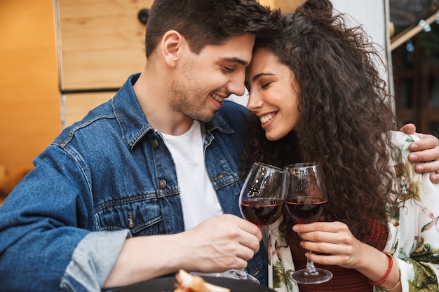 Retrato de casal romântico homem e mulher bebendo vinho tinto enquanto se abraçam perto do trailer ao ar livre