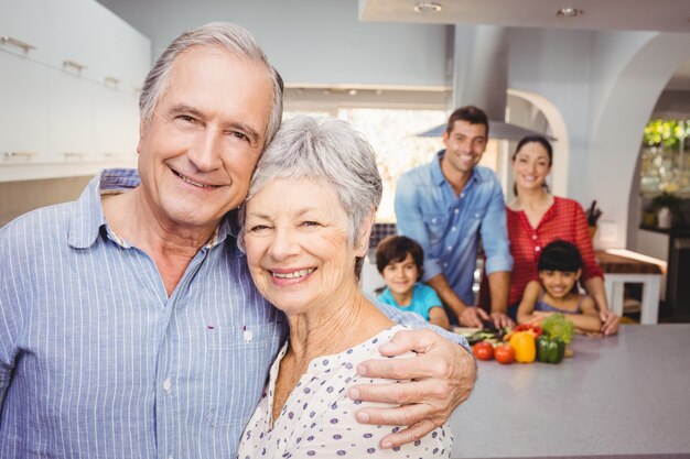 Retrato de casal sênior com a família preparando comida no fundo