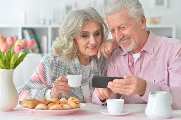 Retrato de casal sênior feliz com smartphone bebendo chá