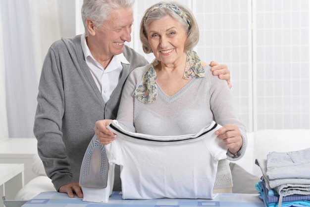 Retrato de casal sênior feliz durante passar roupa em casa