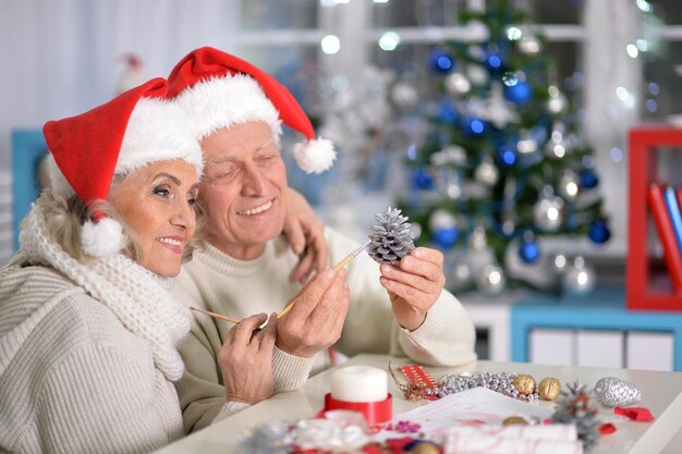 Retrato de casal sênior feliz em chapéus de Papai Noel se preparando para o Natal ou Ano Novo