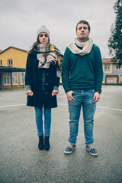 Retrato de casal sério, vestindo roupas de inverno, em pé ao ar livre em um dia frio e chuvoso