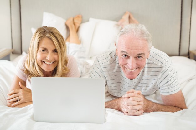 Retrato de casal sorridente, deitada na cama e usando o laptop