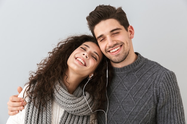 Retrato de casal sorridente, homem e mulher, ouvindo música junto com fones de ouvido, isolado sobre uma parede cinza