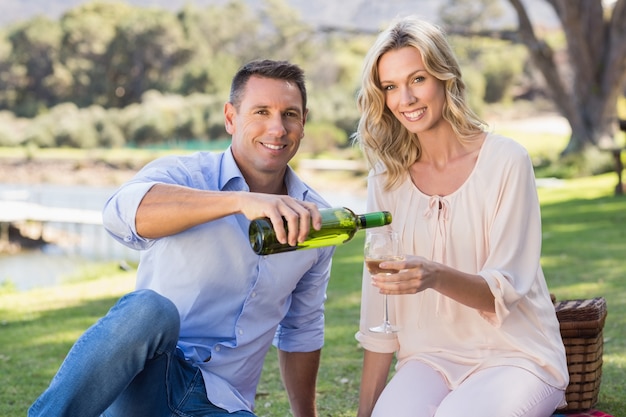 Retrato de casal sorridente sentado e derramando vinho no copo