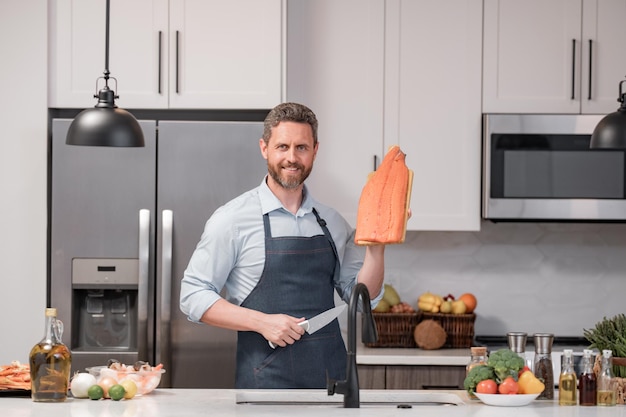 Retrato de chef homem em avental de cozinheiro preparando salmão de refeição natural fresco na cozinha bonito alegre