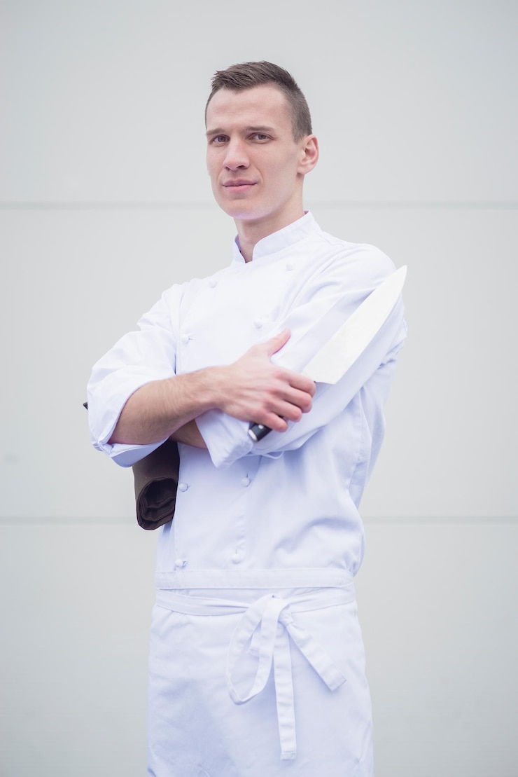 Foto retrato de chef segurando uma faca de cozinha enquanto está de pé contra a parede