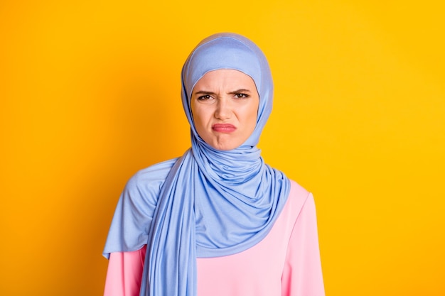 Retrato de close-up de atraente muslimah caprichosa e descontente usando hijab perseguir os lábios isolados em um fundo de cor amarelo brilhante