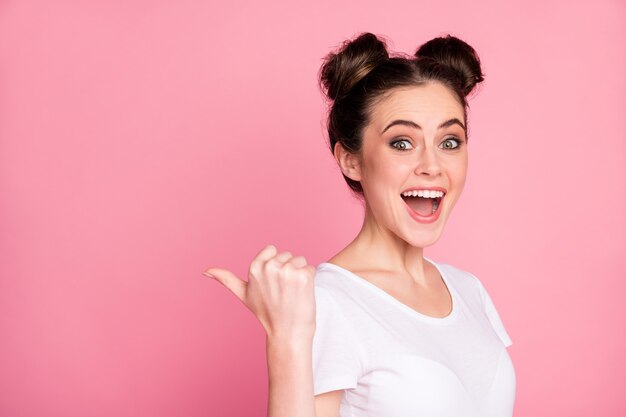 Retrato de close-up de menina alegre apontando o polegar mostrando anúncio isolado sobre fundo rosa