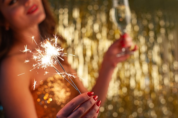 Foto retrato de close-up de mulher caucasiana em vestido de ouro mulher jovem bebe champanhe e segurando diamante na festa sobre fundo dourado brilhante, foco seletivo