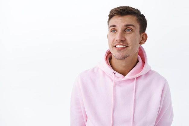 Retrato de close-up de um cara loiro bonito com olhos azuis em um capuz rosa, olhando no canto superior esquerdo com um sorriso sonhador de satisfação