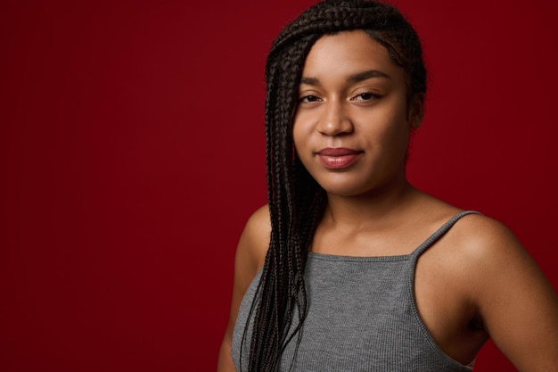 Retrato de close-up de uma jovem africana encantadora com dreadlocks tradicionais elegantes, um sorriso fofo olhando para a câmera, isolado sobre um fundo vermelho com espaço de cópia