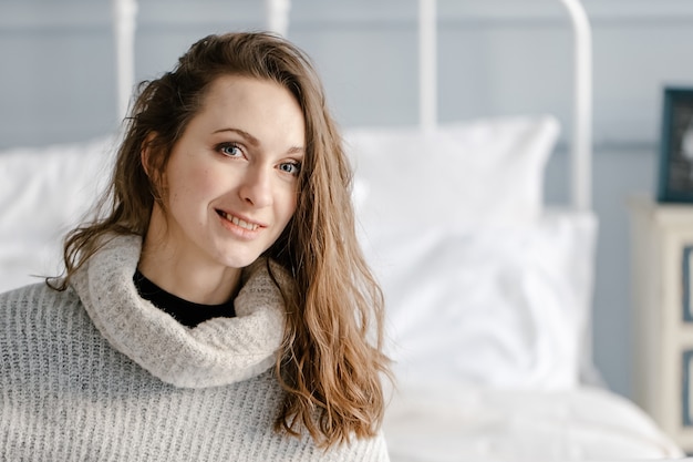 Retrato de close-up de uma jovem muito sorridente com um suéter aconchegante relaxando no quarto em casa