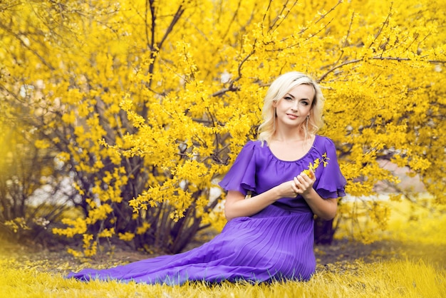 Retrato de close-up de uma menina com maquiagem profissional. mulher linda em um vestido roxo com forsítia florescendo.