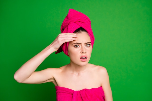 Retrato de close-up de uma senhora atraente desapontada usando turbante de toalha na cabeça, tocando a pele oleosa na testa isolada em um fundo de cor verde viva