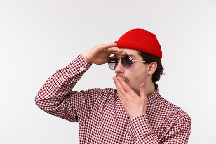Foto retrato de close-up do homem caucasiano chocado e sem palavras de gorro vermelho e óculos de sol, ofegante boca de descrença e tremeu, olhar para longe, encontrou algo chocante, ficar parede branca