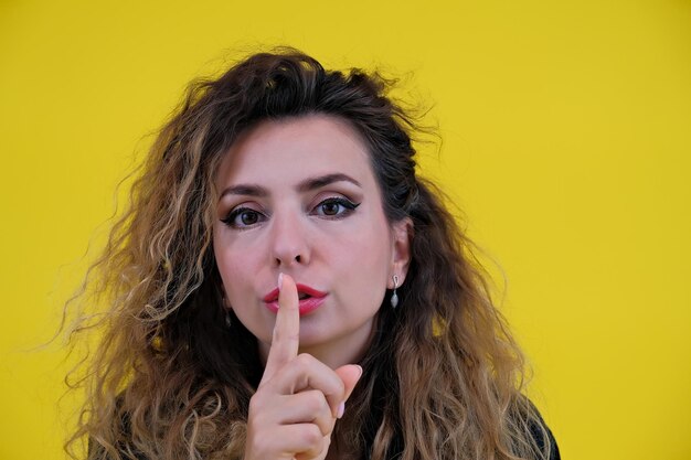 Retrato de close-up linda garota em uma mulher de fundo amarelo mostrando a garota do silêncio do dedo mostrando o sinal de shh manter segredo
