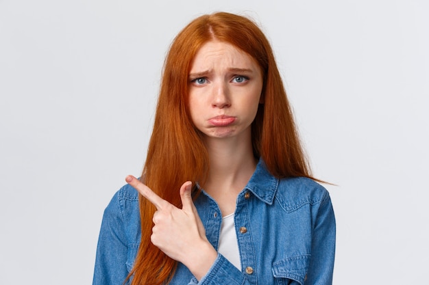 Retrato de close-up, ruiva insegura, chateada e sombria, chorando, sentindo-se injusta e com ciúmes, reclamando, pedindo favor, quer comprar algo pedir permissão, apontando para a esquerda