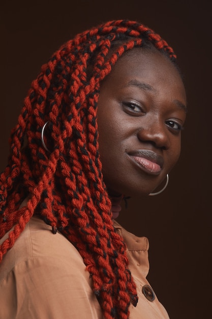 Retrato de close-up vertical de uma jovem afro-americana elegante com cabelo trançado, olhando para a câmera enquanto posa com segurança no estúdio