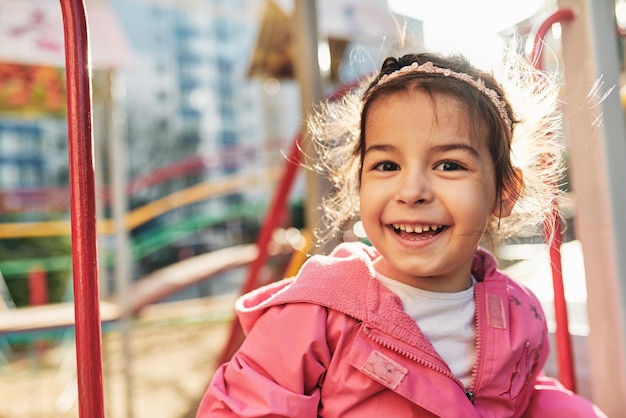 Retrato de closeup ao ar livre de menina feliz sorrindo amplamente vestindo roupa rosa posando do lado de fora Criança alegre brincando no playground no parque Conceito de infância e educação feliz