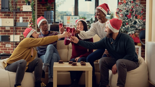 Retrato de colegas de trabalho tilintando copos de vinho durante a festa de natal do escritório, fazendo brinde para comemorar o feriado sazonal. Beber álcool e dizer aplausos na festa de inverno com decoração.