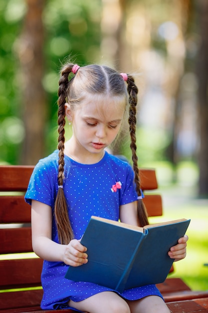 Retrato de colegial em um livro de leitura do banco. Parque da cidade de fundo.