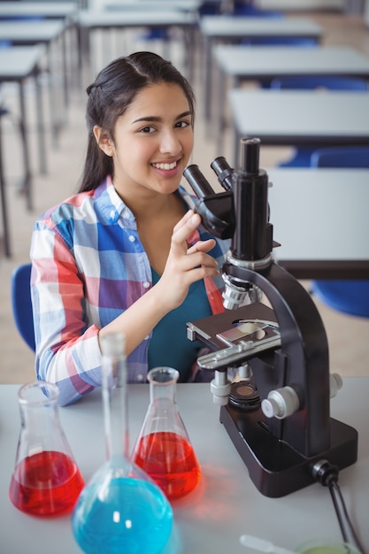 Retrato de colegial experimentando no microscópio em laboratório