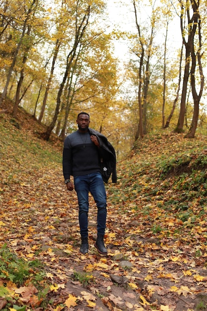 Foto retrato de comprimento completo de homem negro africano em suéter de pé na calçada no parque durante o outono