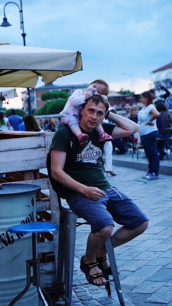 Foto retrato de comprimento completo de um jovem carregando a filha enquanto estava sentado no mercado