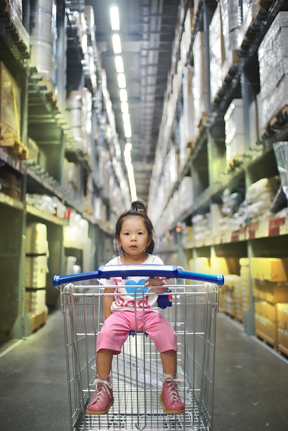 Foto retrato de comprimento completo de uma menina bonita sentada no carrinho de compras no shopping