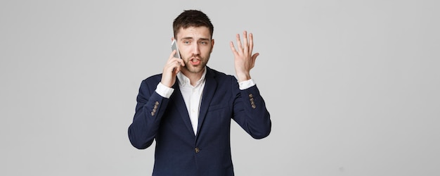 Retrato de conceito de negócios jovem e bonito homem de negócios zangado de terno falando no telefone olhando para a câmera Fundo branco