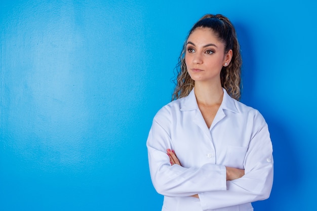 Retrato de confiante com sorriso radiante e qualificado, experiente e inteligente médico inteligente, vestindo roupa formal branca, ela está de pé com os braços cruzados, isolado no fundo azul