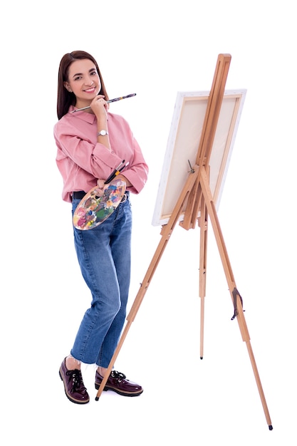 Foto retrato de corpo inteiro da artista jovem bonita com cavalete, paleta e pintura a pincel isolado no fundo branco