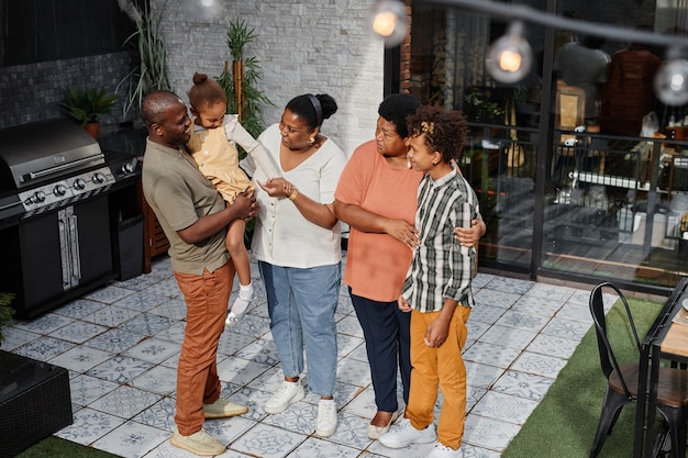 Retrato de corpo inteiro da família afro-americana moderna conversando no terraço durante a festa de churrasco ...