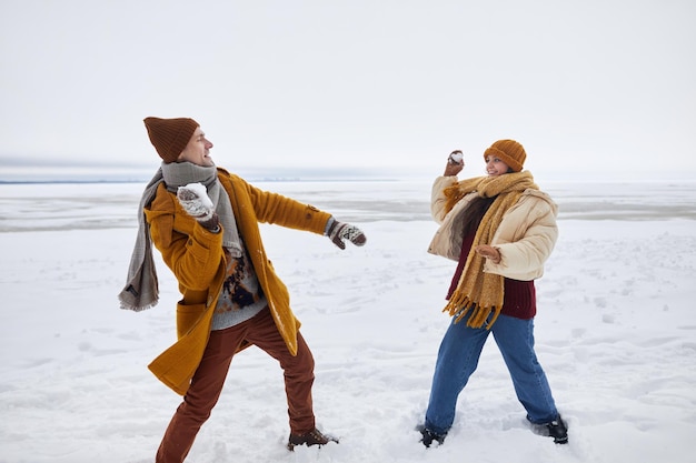 Retrato de corpo inteiro de casal jogando bola de neve ao ar livre no espaço de cópia de inverno