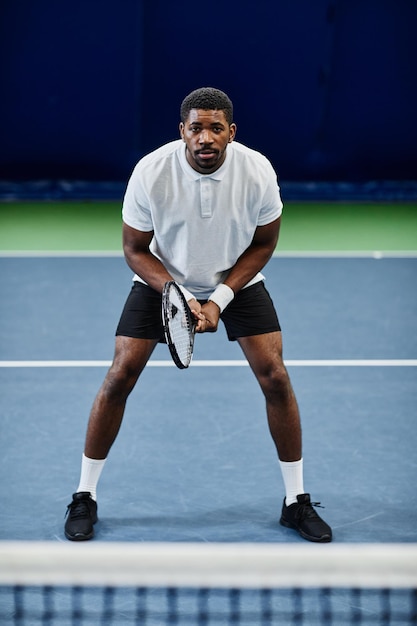 Retrato de corpo inteiro de desportista negro profissional jogando tênis na quadra coberta