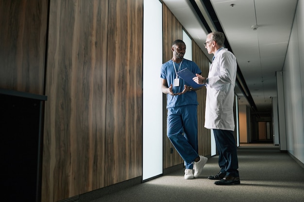 Retrato de corpo inteiro de dois médicos conversando em pé na sala da clínica, copie o espaço