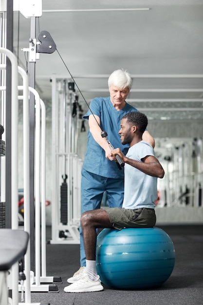 Retrato de corpo inteiro de especialista em fisioterapia ajudando jovem afro-americano fazendo reabilitação